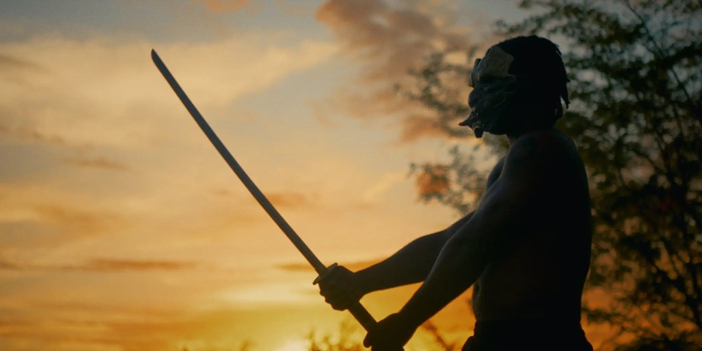 Silhouette of a person holding a sword against a sunset sky, wearing a mask.